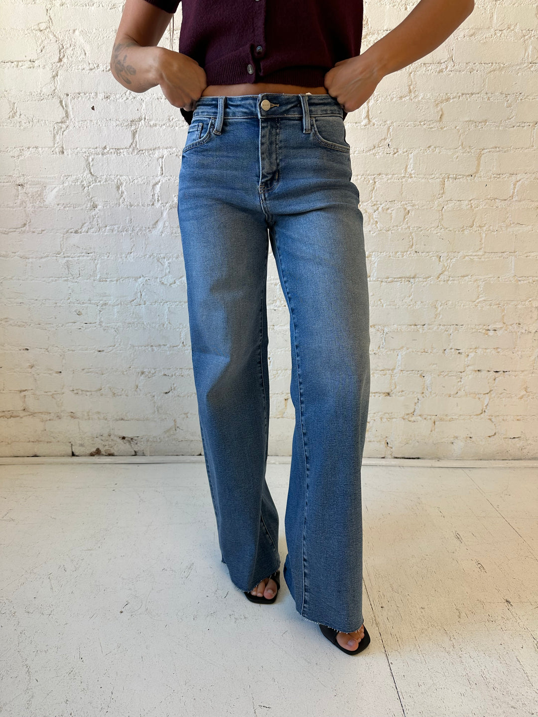 Woman wearing medium wash wide leg jeans with a raw hem, and burgundy sweater top. 