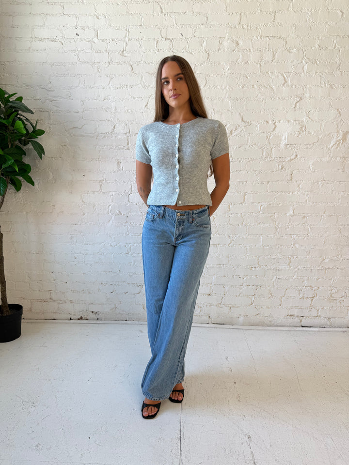 Woman wearing grey short sleeve knit button down top with medium wash jeans. 
