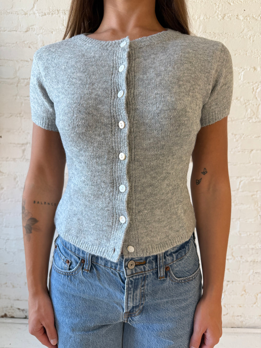 Woman wearing grey short sleeve knit button down top with medium wash jeans. 