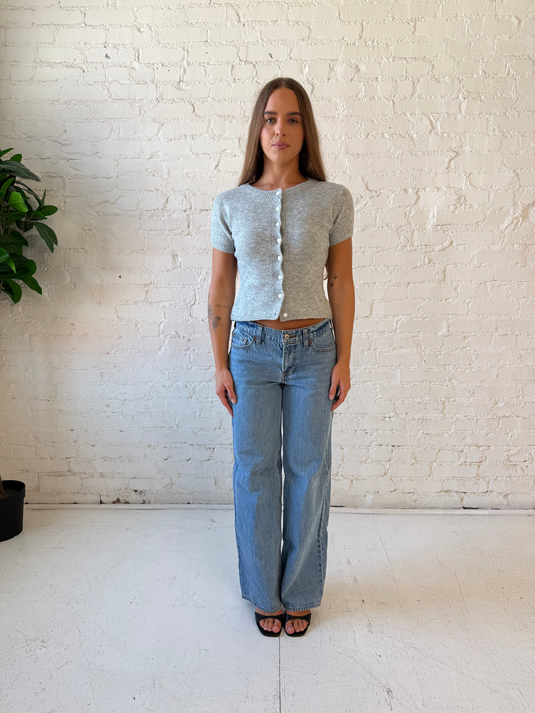 Woman wearing grey short sleeve knit button down top with medium wash jeans. 