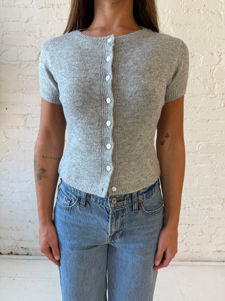 Woman wearing grey short sleeve knit button down top with medium wash jeans. 