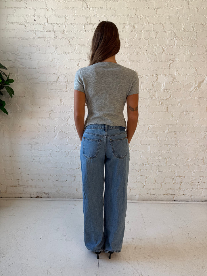 Woman wearing grey short sleeve knit button down top with medium wash jeans. 