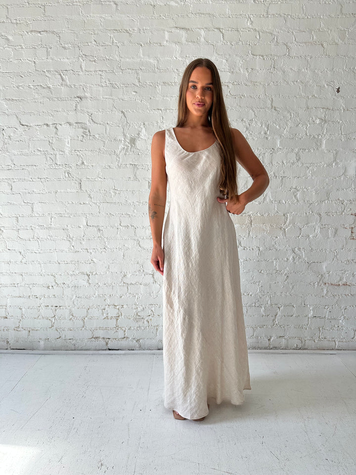 Woman wearing beige linen maxi dress with scoop neckline. 