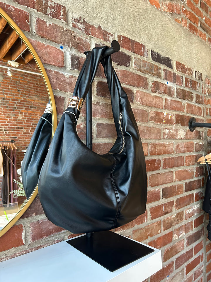 Black faux leather slouchy shoulder bag with gold hardware detail, and zipper closure. 