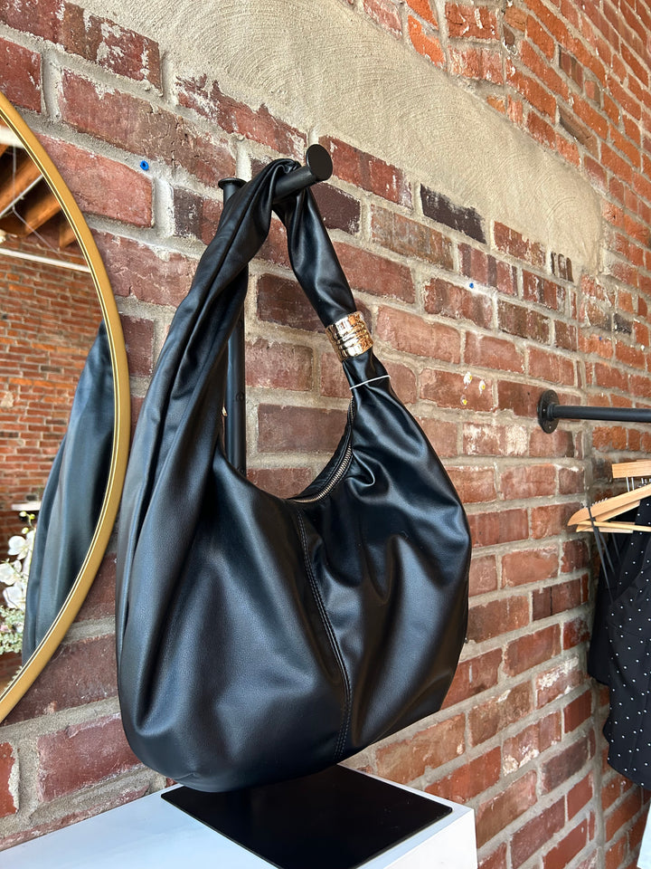 Black faux leather slouchy shoulder bag with gold hardware detail, and zipper closure. 