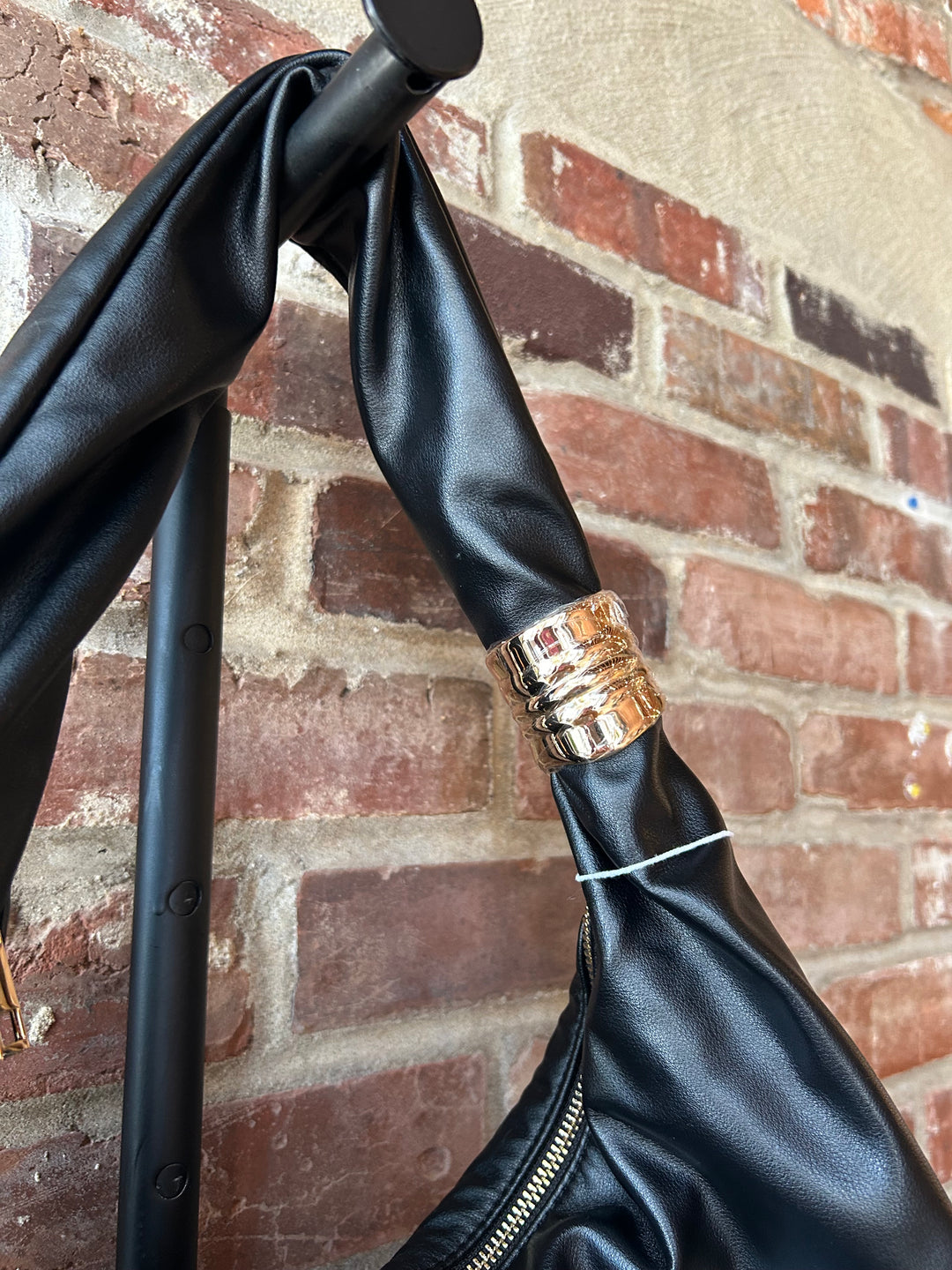 Black faux leather slouchy shoulder bag with gold hardware detail, and zipper closure. 