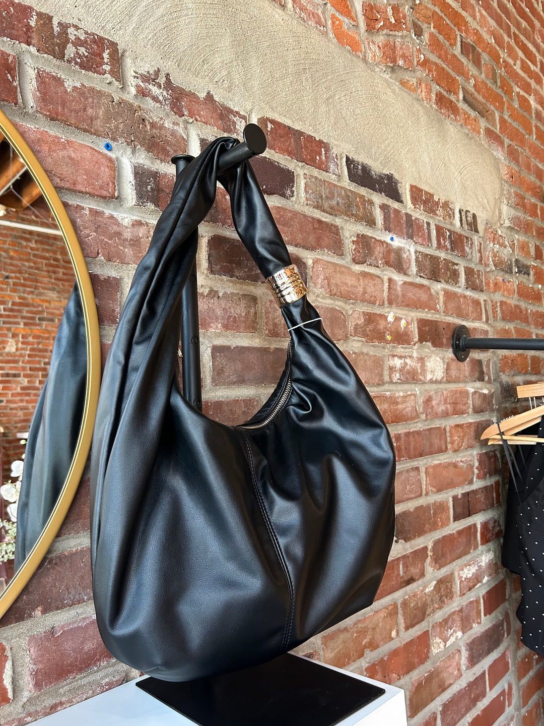 Black faux leather slouchy shoulder bag with gold hardware detail, and zipper closure. 