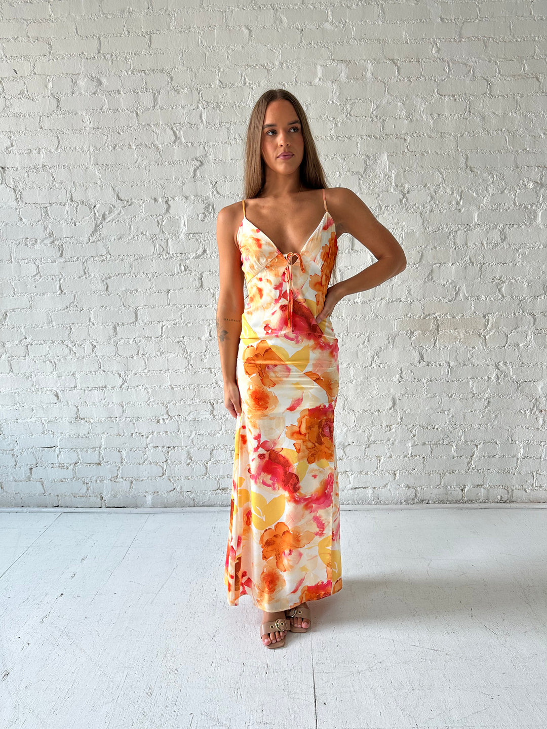 Woman wearing satin floral maxi dress with front tie detail, and side slit. 