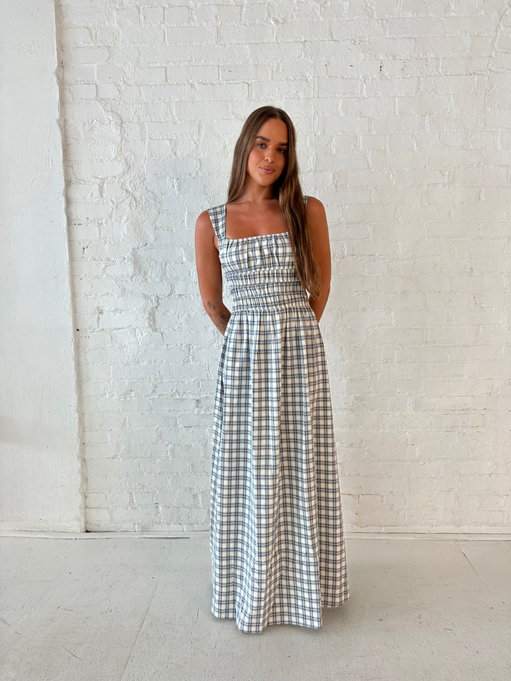 Woman wearing neutral plaid maxi dress with a smocked midsection, and elastic straight neckline 
