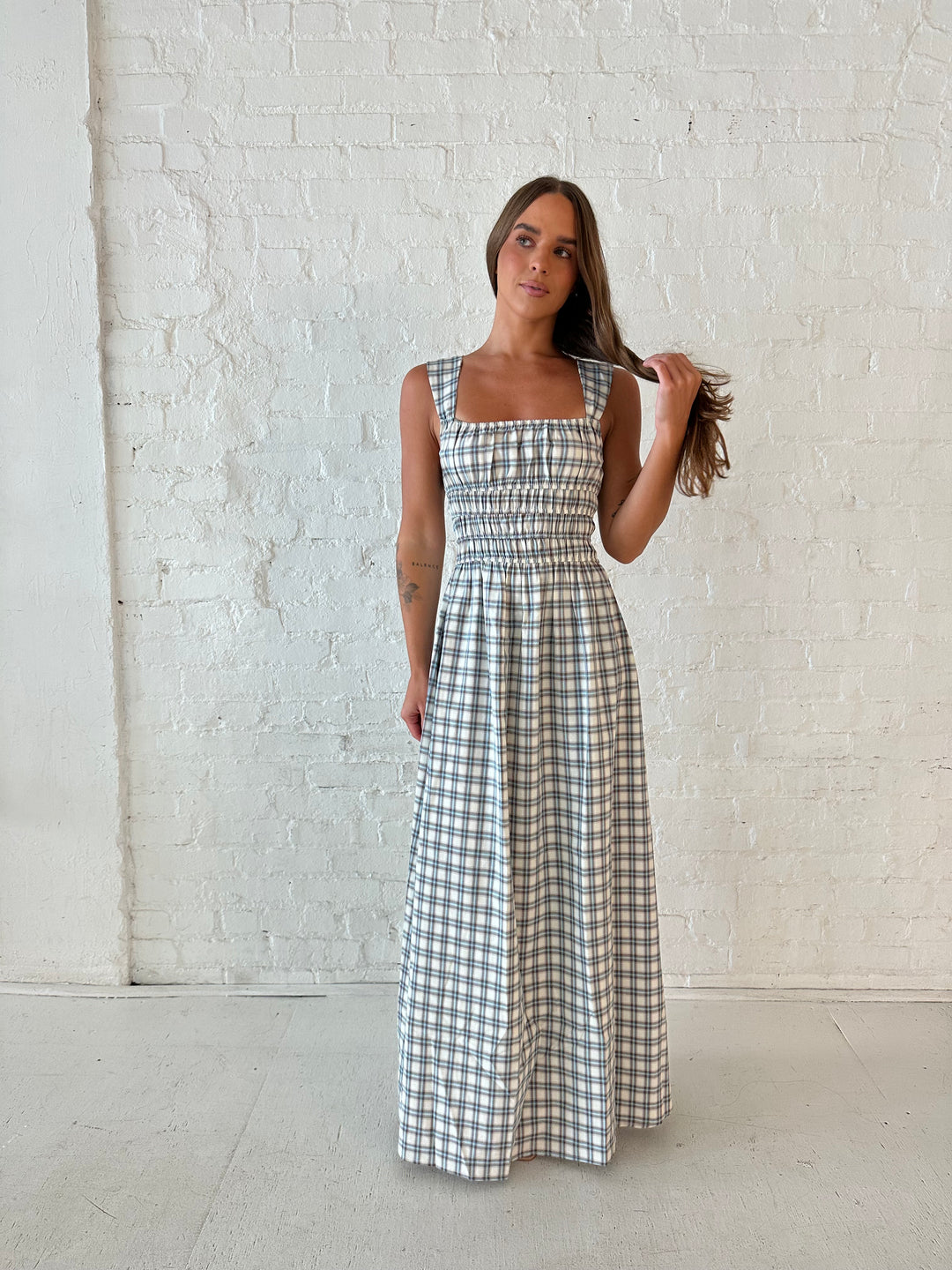 Woman wearing neutral plaid maxi dress with a smocked midsection, and elastic straight neckline 