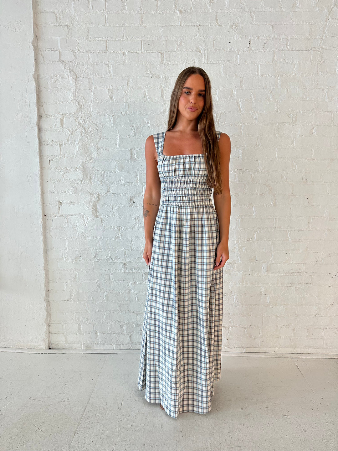 Woman wearing neutral plaid maxi dress with a smocked midsection, and elastic straight neckline 