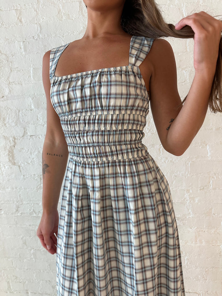 Woman wearing neutral plaid maxi dress with a smocked midsection, and elastic straight neckline 