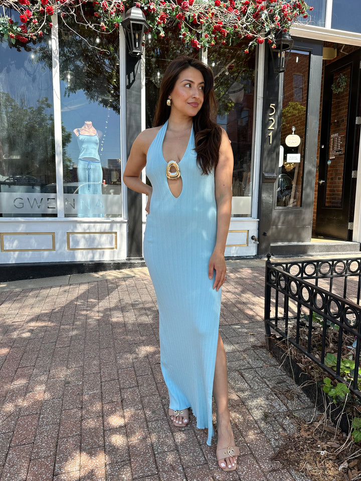 Woman wearing light blue knit maxi dress with plunging neckline, and gold hardware.
