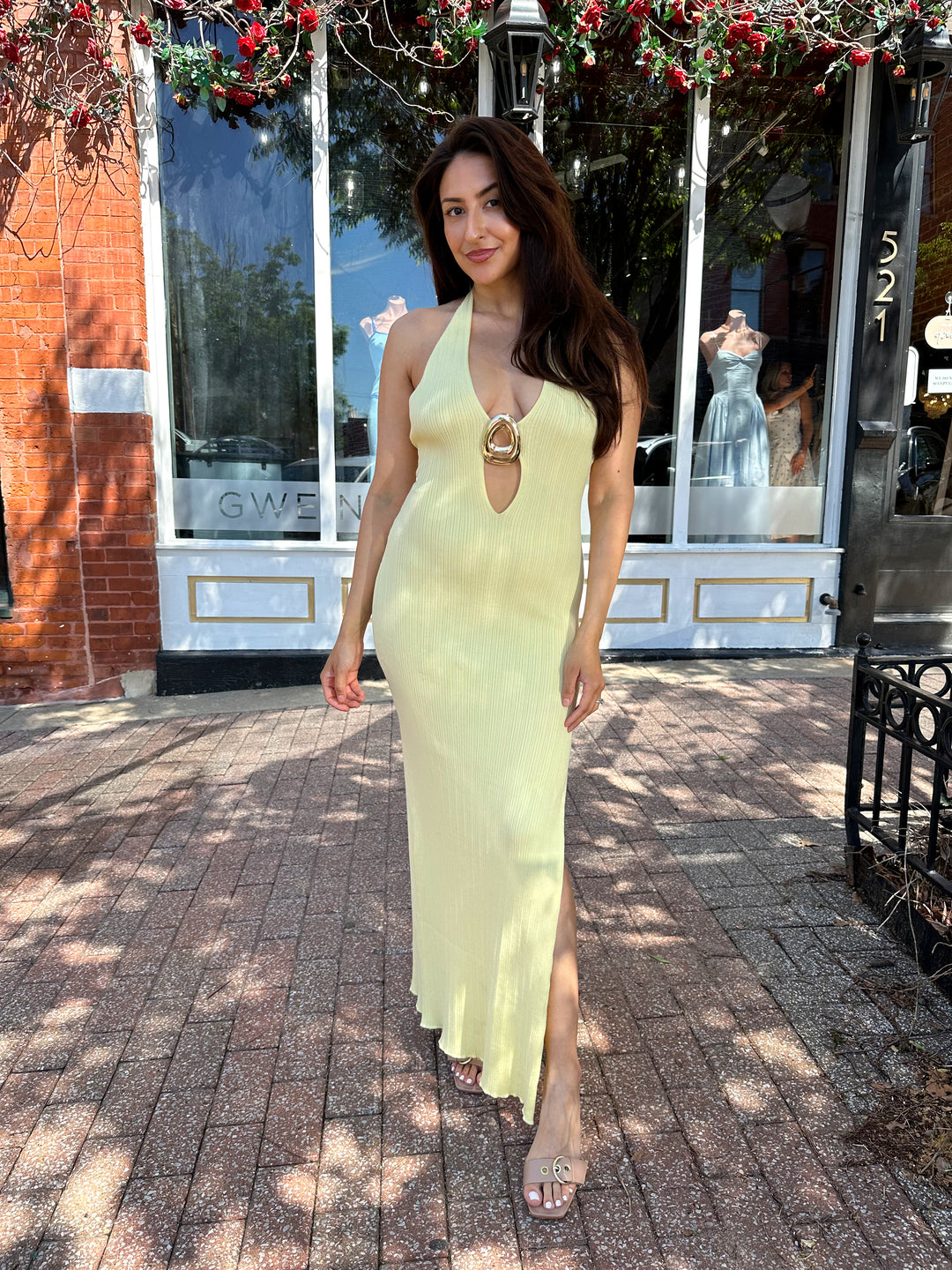 Woman wearing yellow knit maxi dress with plunging neckline, and gold hardware.