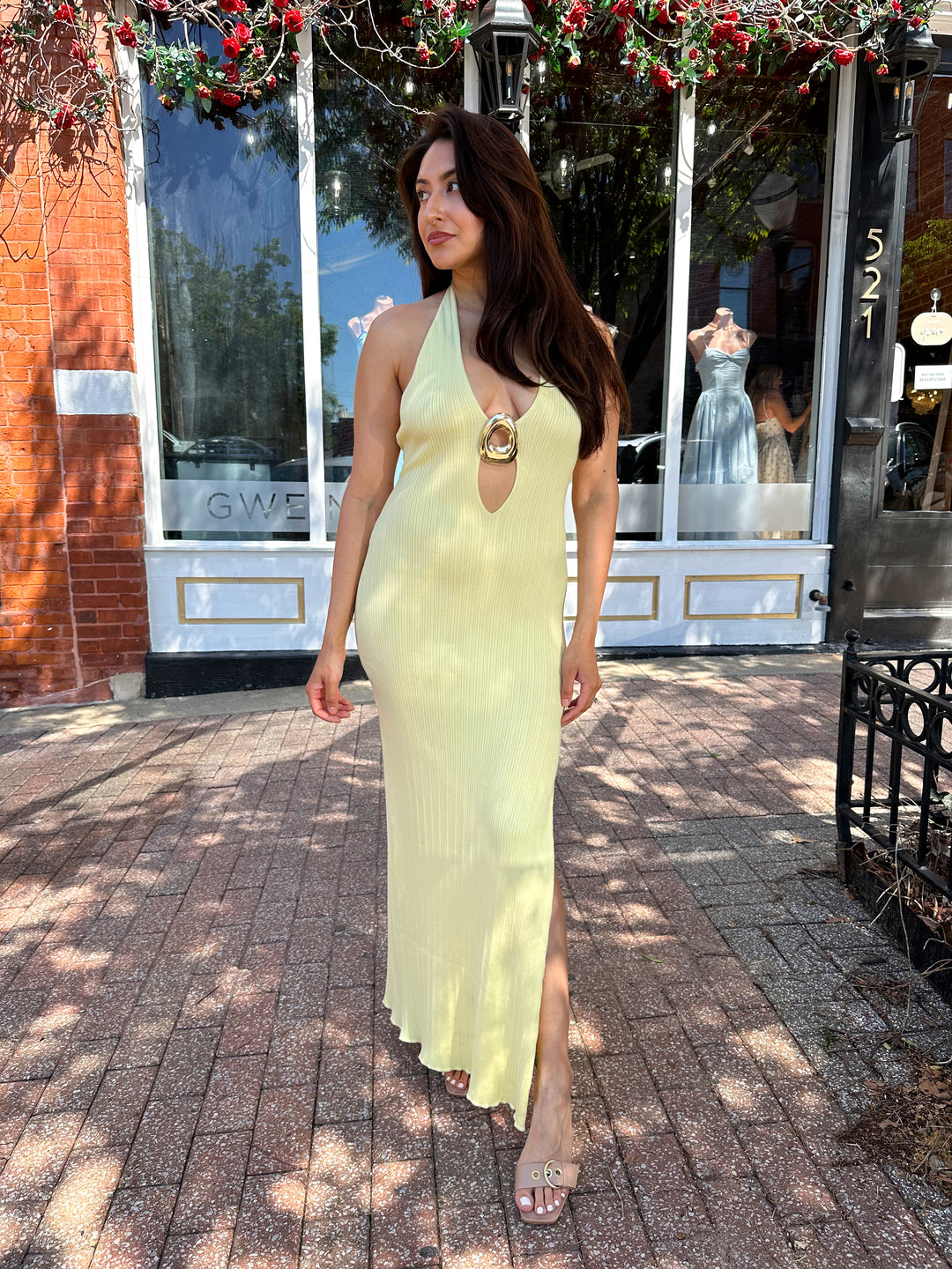 Woman wearing yellow knit maxi dress with plunging neckline, and gold hardware.