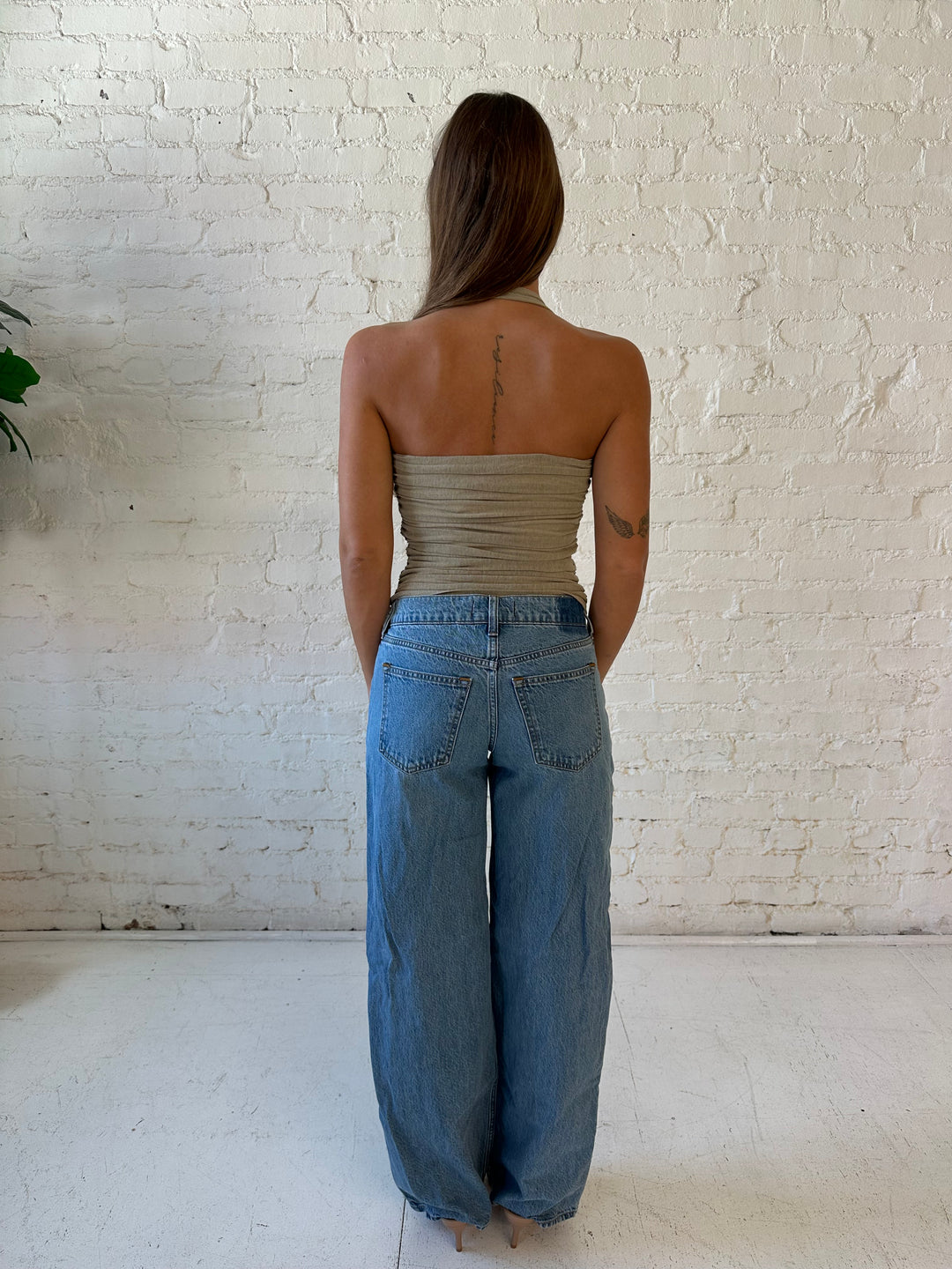 Woman wearing a taupe ruched halter top with medium wash jeans. 