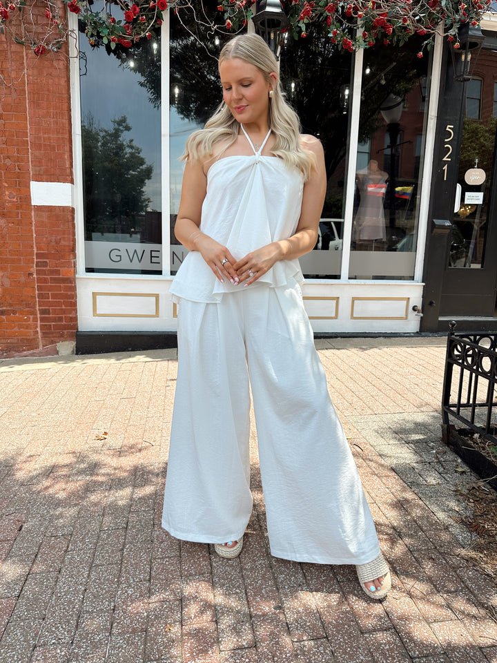 Woman wearing white flowy two piece set with self tie halter top and wide leg pant. 