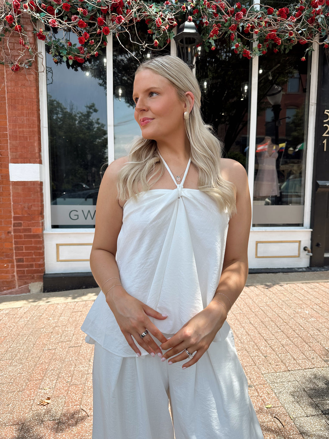 Woman wearing white flowy two piece set with self tie halter top and wide leg pant. 