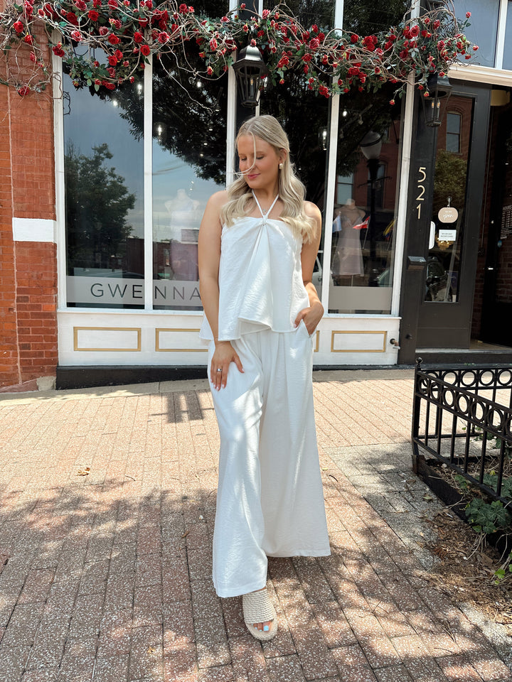 Woman wearing white flowy two piece set with self tie halter top and wide leg pant. 