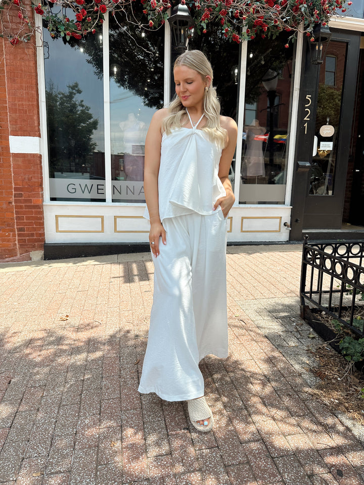 Woman wearing white flowy two piece set with self tie halter top and wide leg pant. 