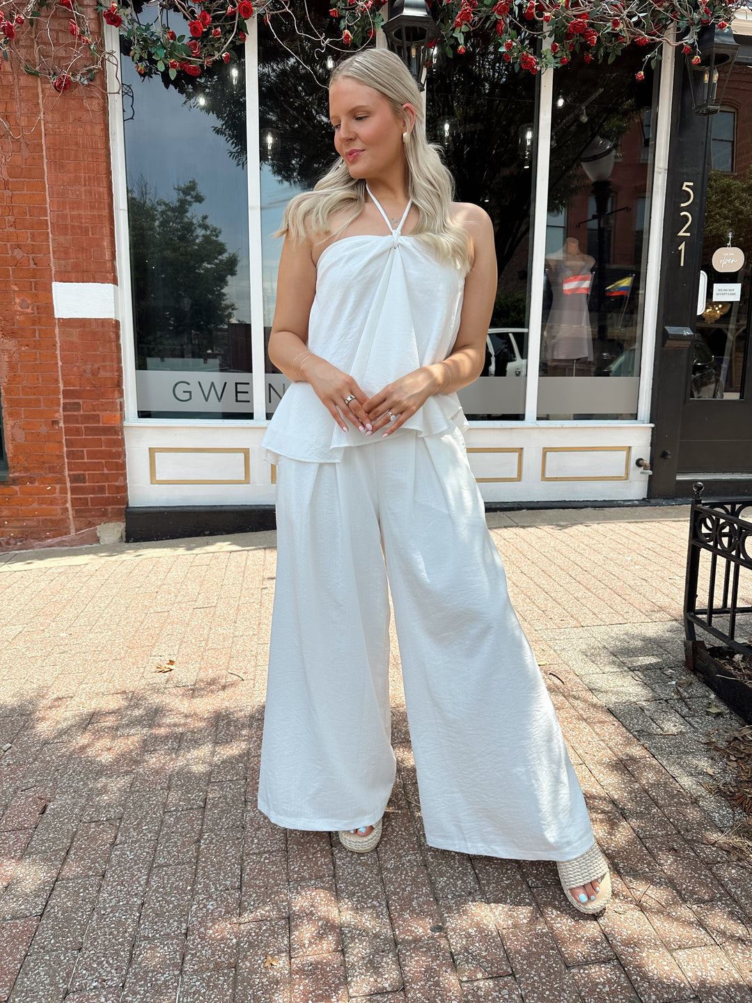 Woman wearing white flowy two piece set with self tie halter top and wide leg pant. 