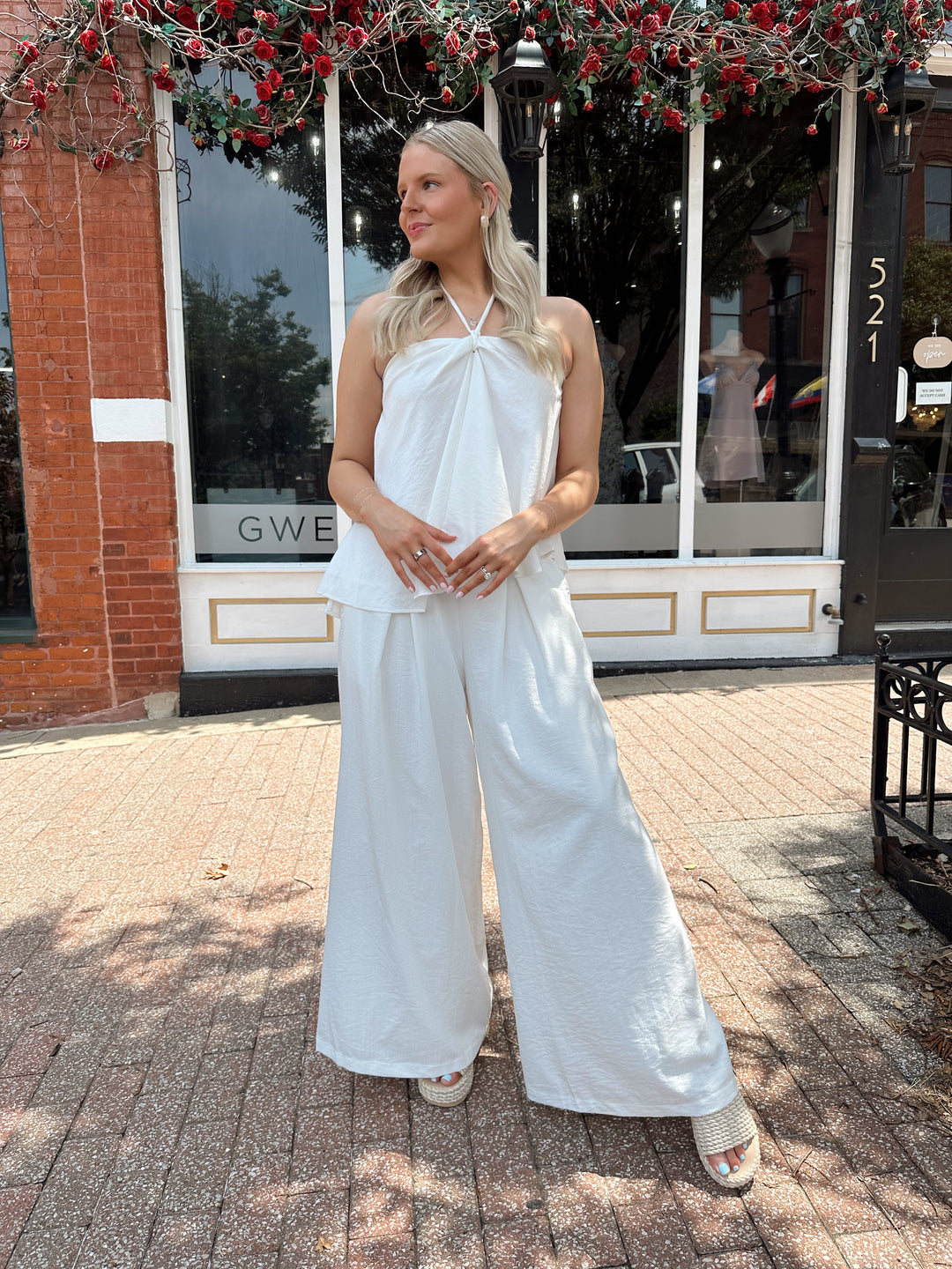 Woman wearing white flowy two piece set with self tie halter top and wide leg pant. 
