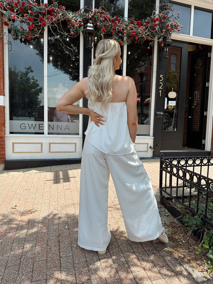 Woman wearing white flowy two piece set with self tie halter top and wide leg pant. 