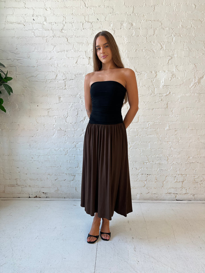 Woman wearing color block midi dress with a black top and brown bottom with ruching details on the side. 
