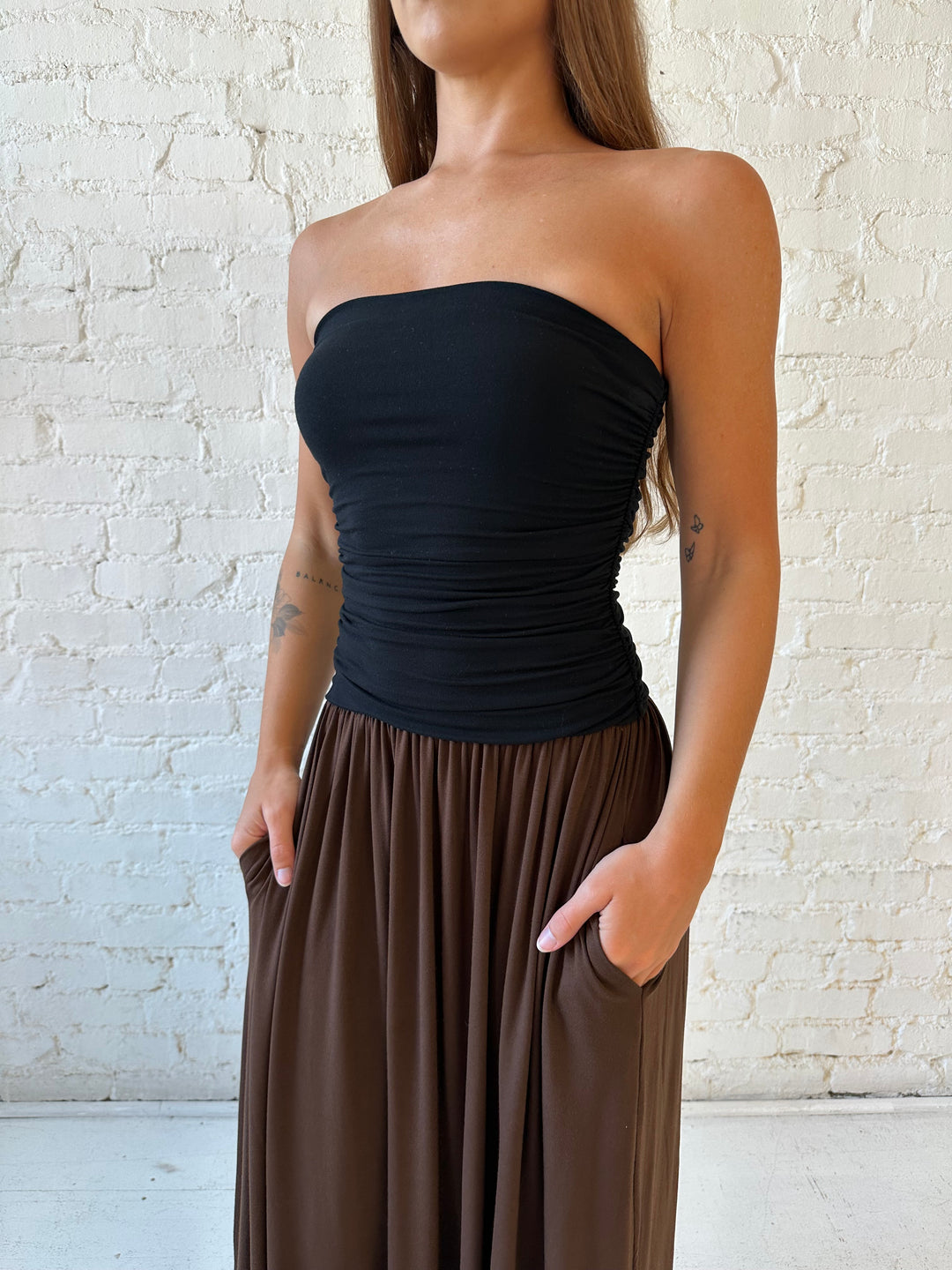 Woman wearing color block midi dress with a black top and brown bottom with ruching details on the side. 