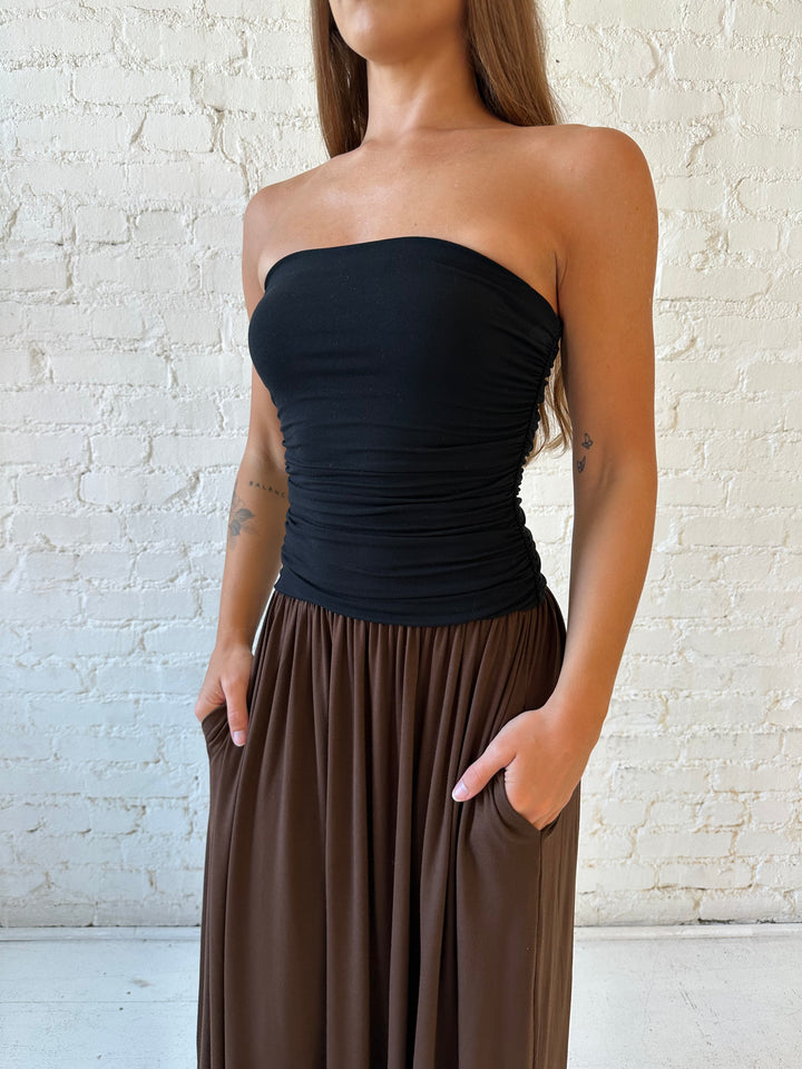 Woman wearing color block midi dress with a black top and brown bottom with ruching details on the side. 