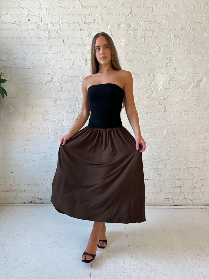 Woman wearing color block midi dress with a black top and brown bottom with ruching details on the side. 