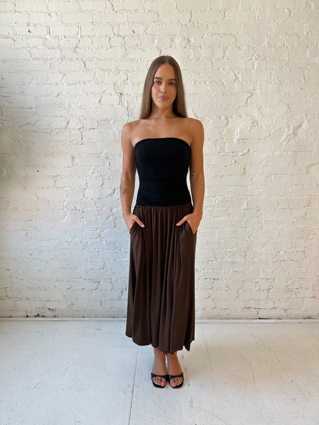 Woman wearing color block midi dress with a black top and brown bottom with ruching details on the side. 