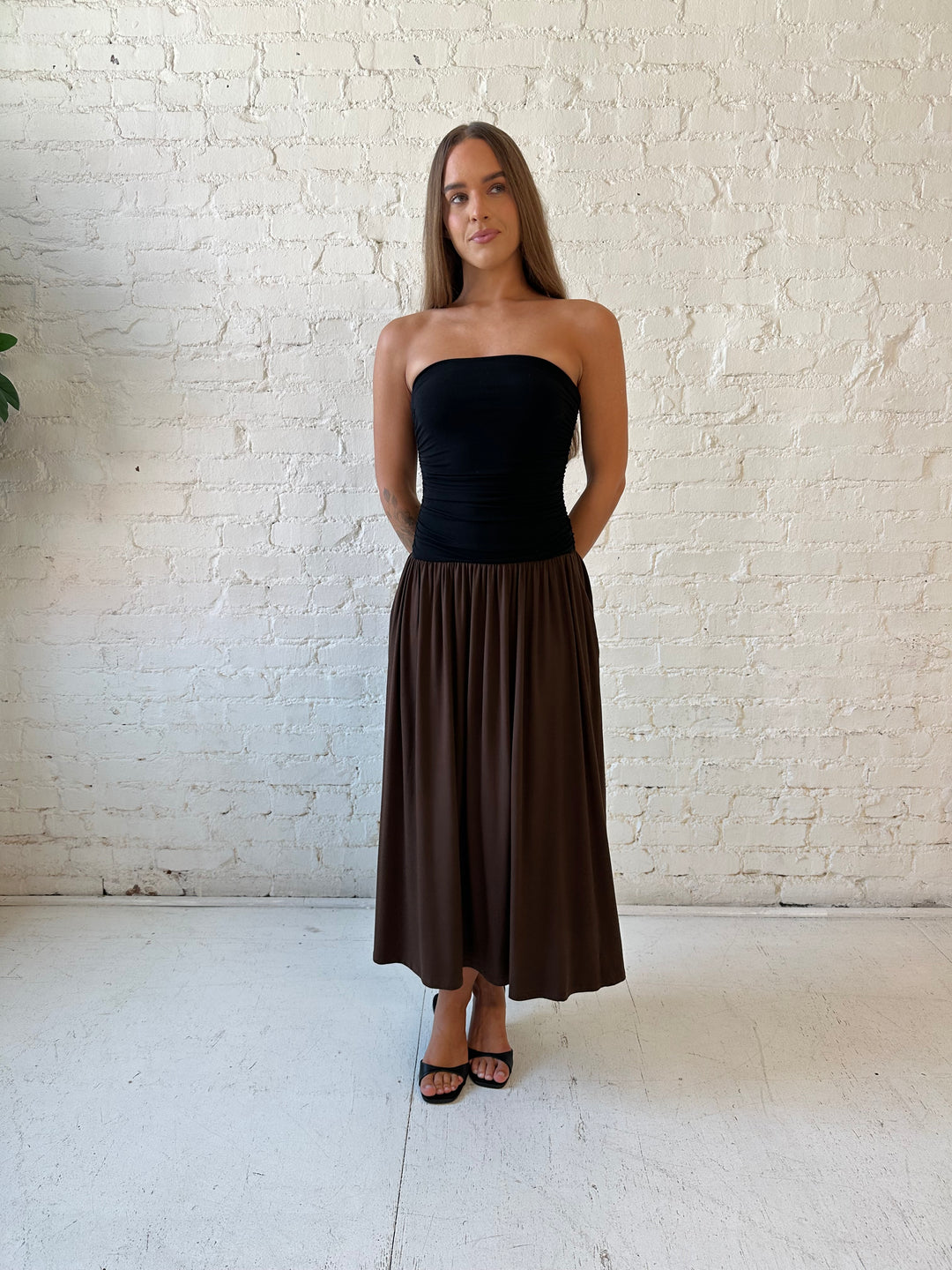 Woman wearing color block midi dress with a black top and brown bottom with ruching details on the side. 