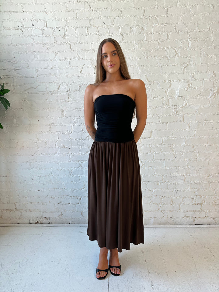 Woman wearing color block midi dress with a black top and brown bottom with ruching details on the side. 