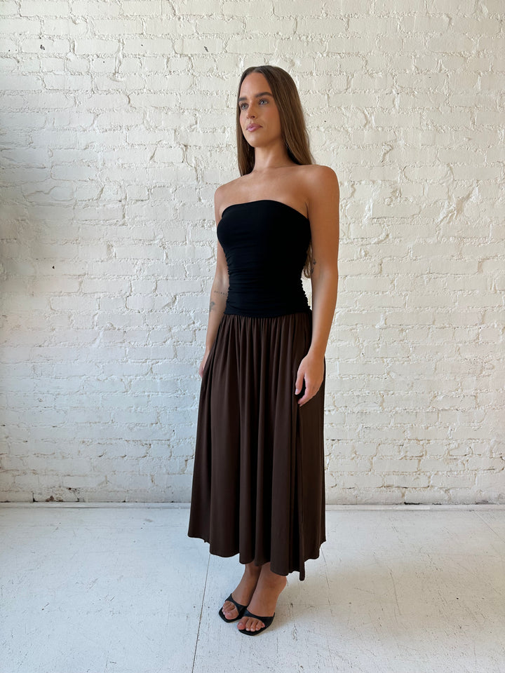 Woman wearing color block midi dress with a black top and brown bottom with ruching details on the side. 