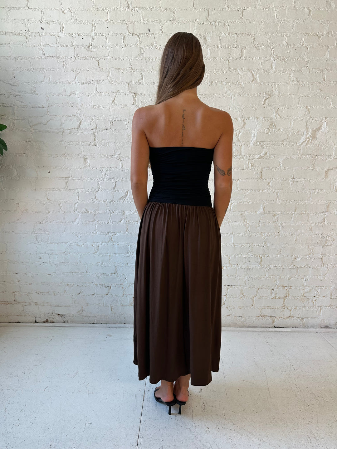 Woman wearing color block midi dress with a black top and brown bottom with ruching details on the side. 
