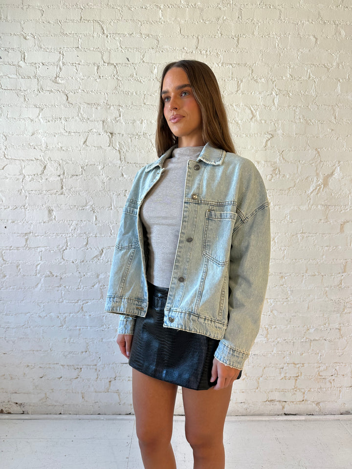 Woman wearing light wash relaxed fit denim jacket with high waisted mini skort and neutral top.