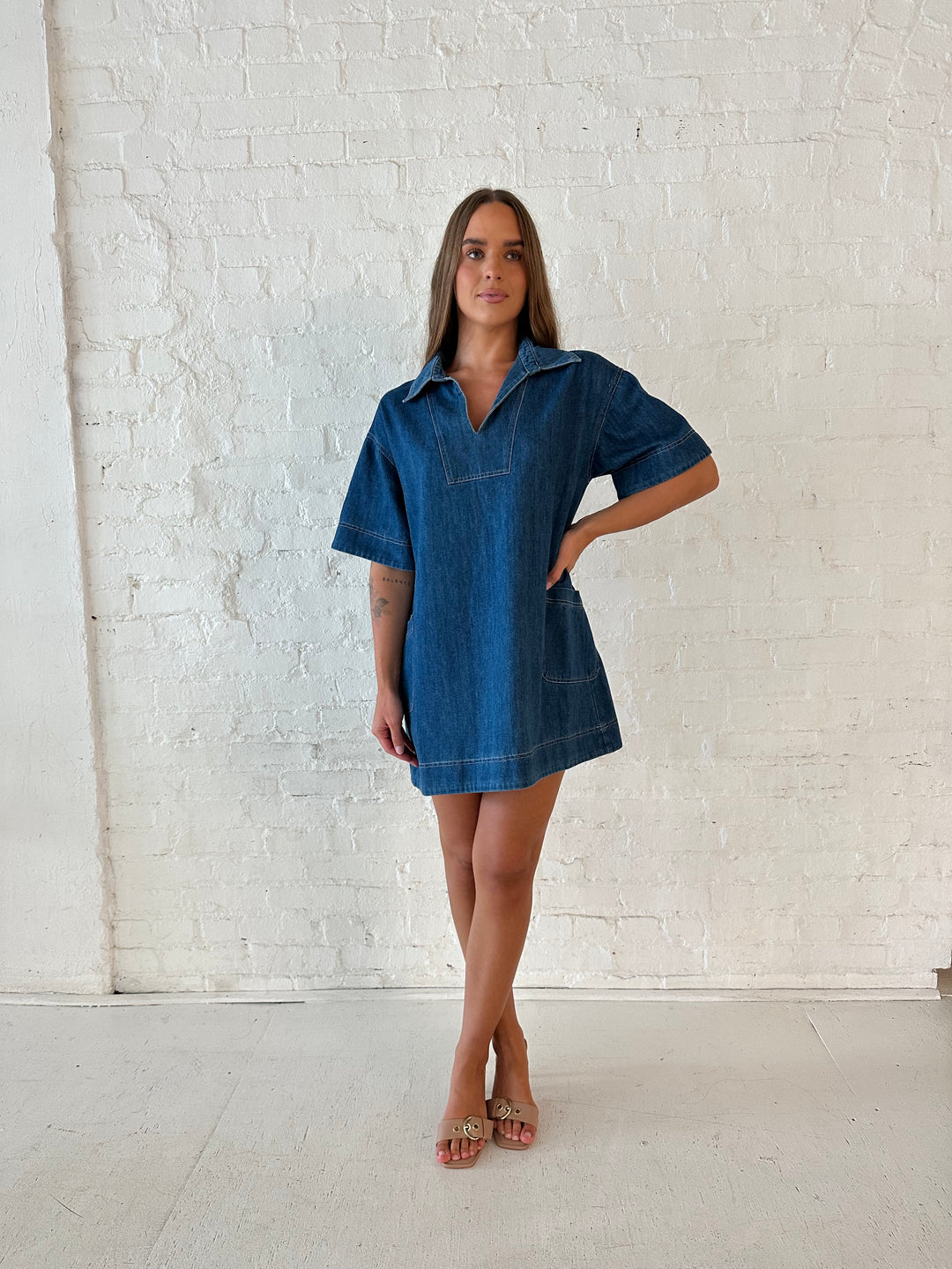 Woman wearing dark wash shift style mini dress with short sleeves, collar detailing, and pockets. 