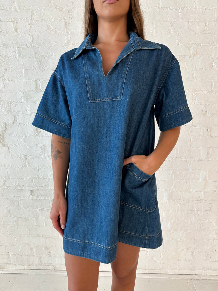 Woman wearing dark wash shift style mini dress with short sleeves, collar detailing, and pockets. 