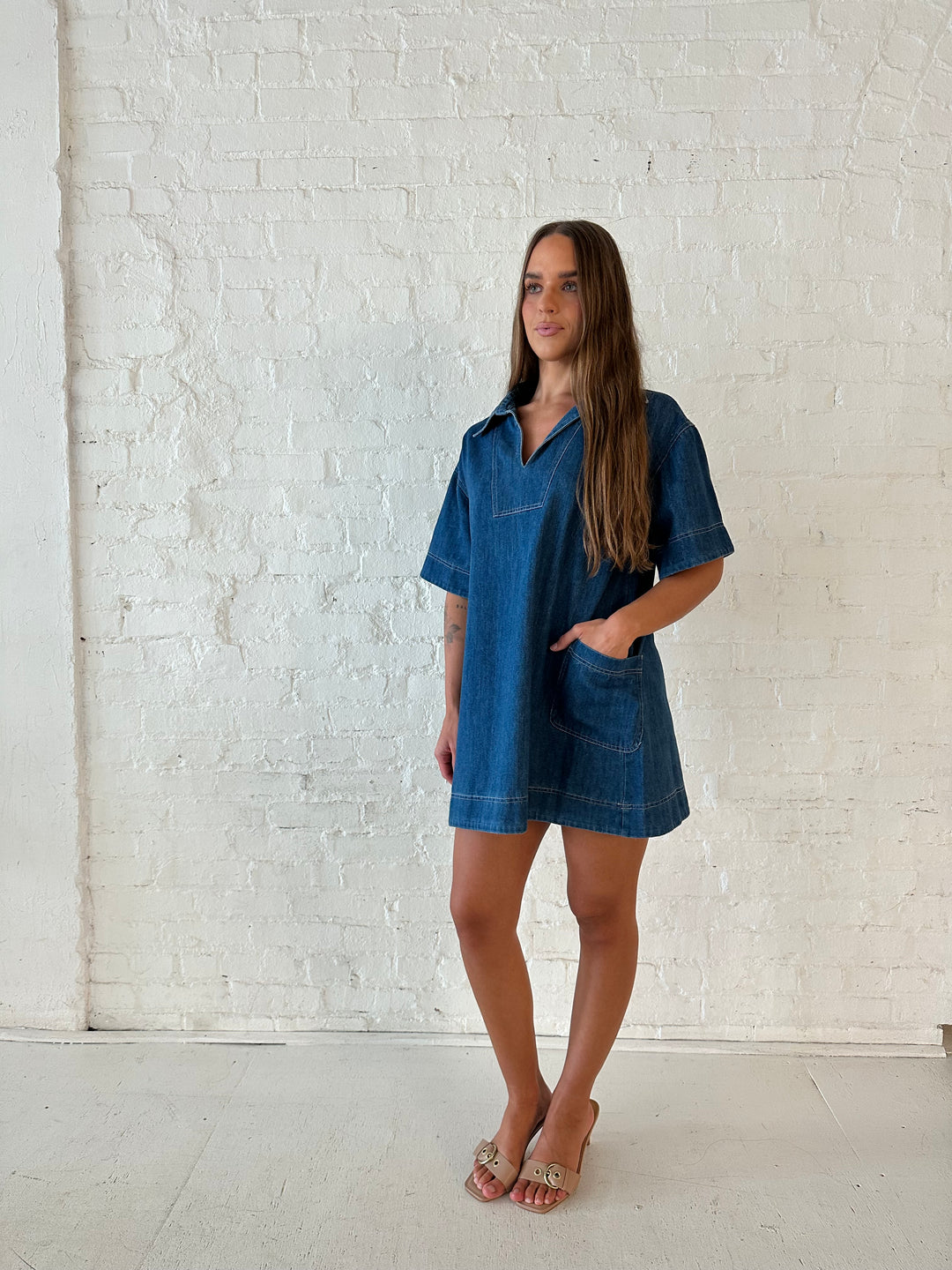 Woman wearing dark wash shift style mini dress with short sleeves, collar detailing, and pockets. 