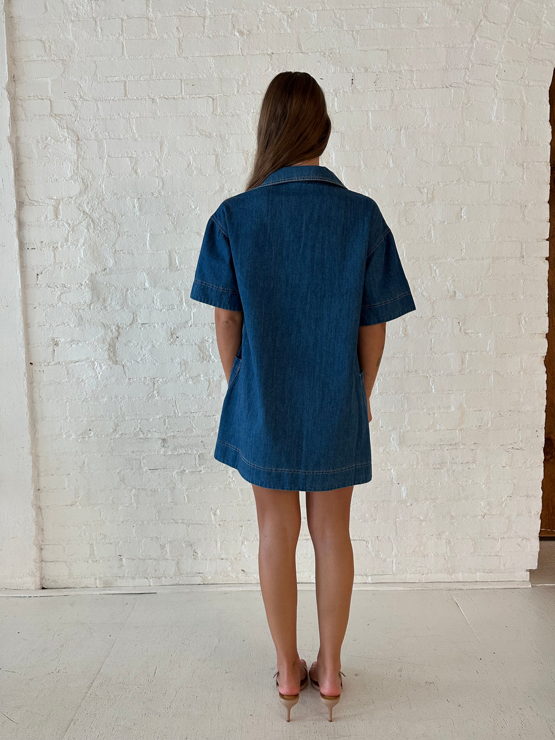 Woman wearing dark wash shift style mini dress with short sleeves, collar detailing, and pockets. 