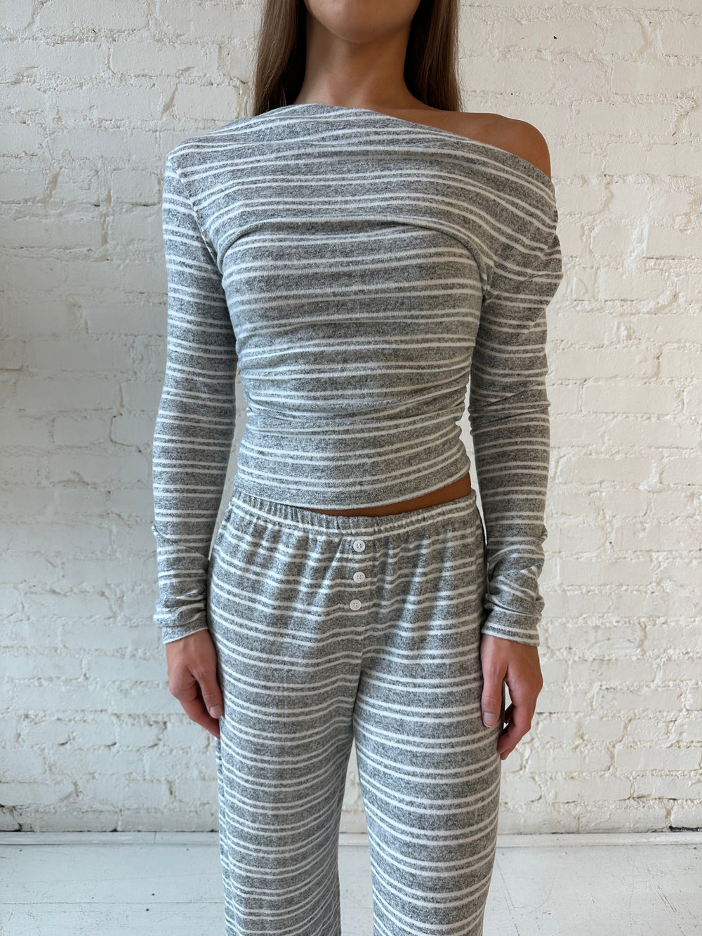 Woman wearing grey and white striped two piece lounge set with long sleeve, off the shoulder top. 