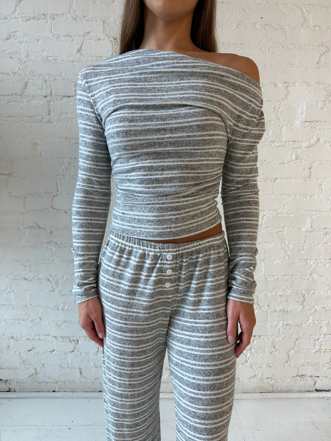 Woman wearing grey and white striped two piece lounge set with long sleeve, off the shoulder top. 