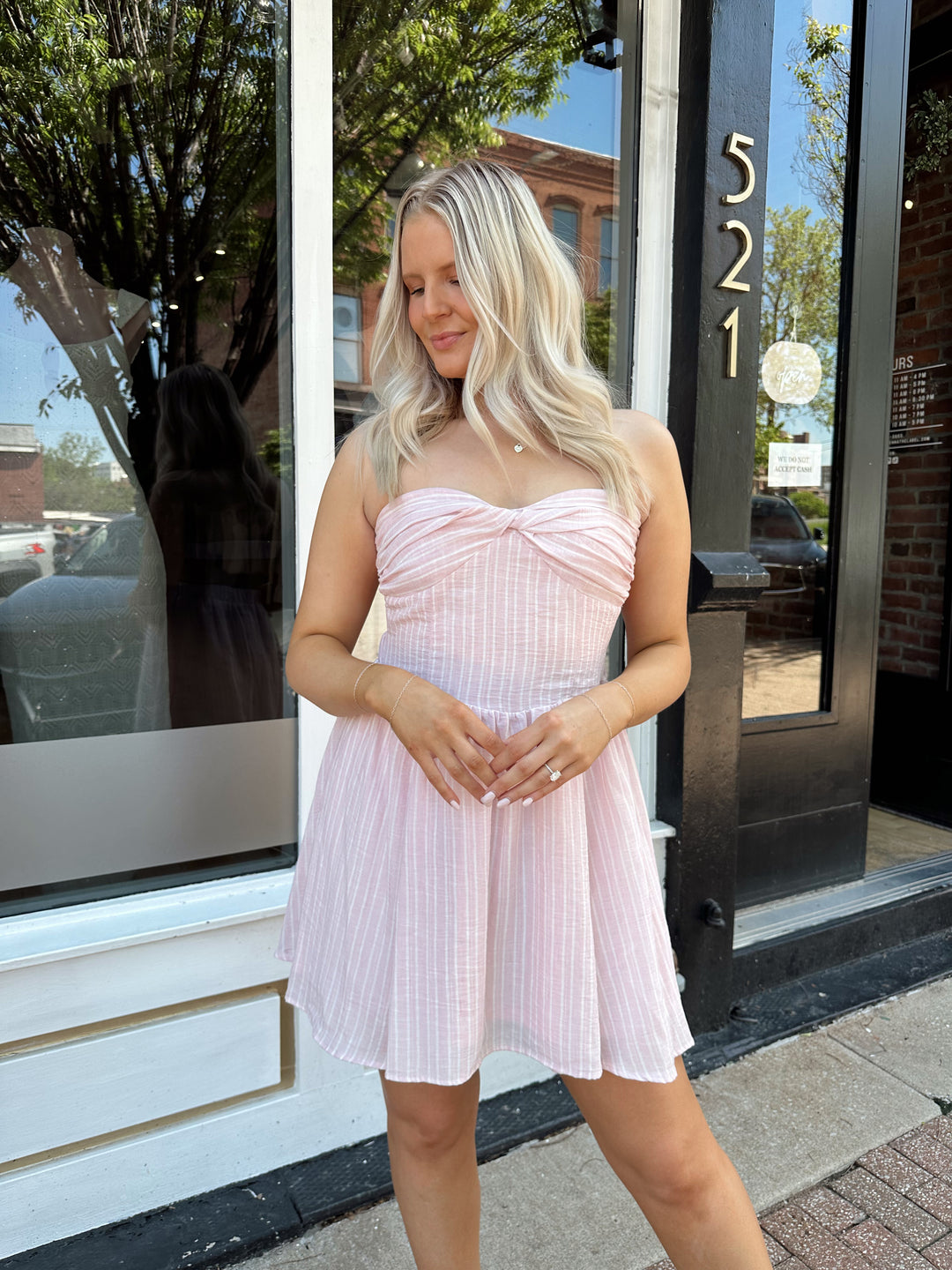 Woman wearing light pink striped strapless mini dress with open back. 