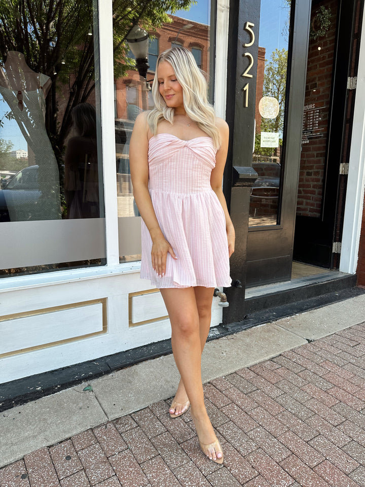 Woman wearing light pink striped strapless mini dress with open back. 