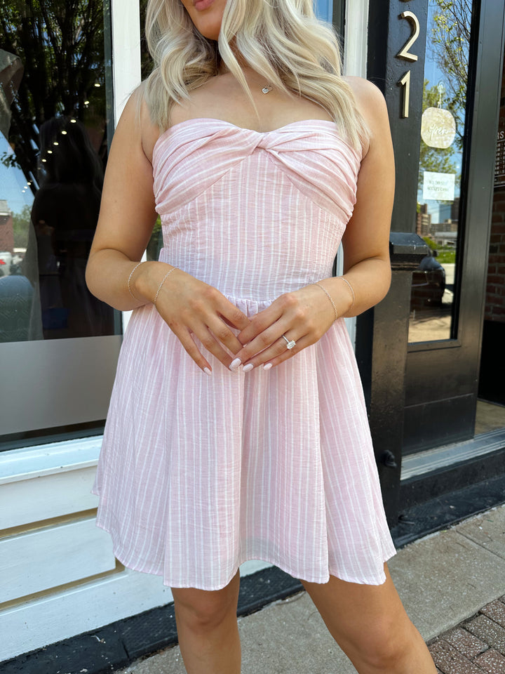 Woman wearing light pink striped strapless mini dress with open back. 