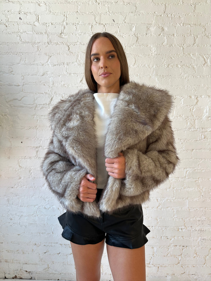 Woman wearing oversized boxy taupe faux fur coat with high waisted faux leather shorts.