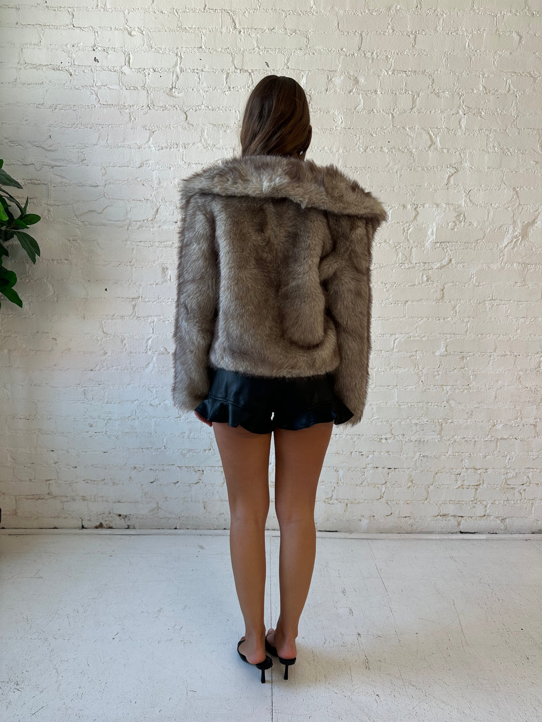 Woman wearing oversized boxy taupe faux fur coat with high waisted faux leather shorts.