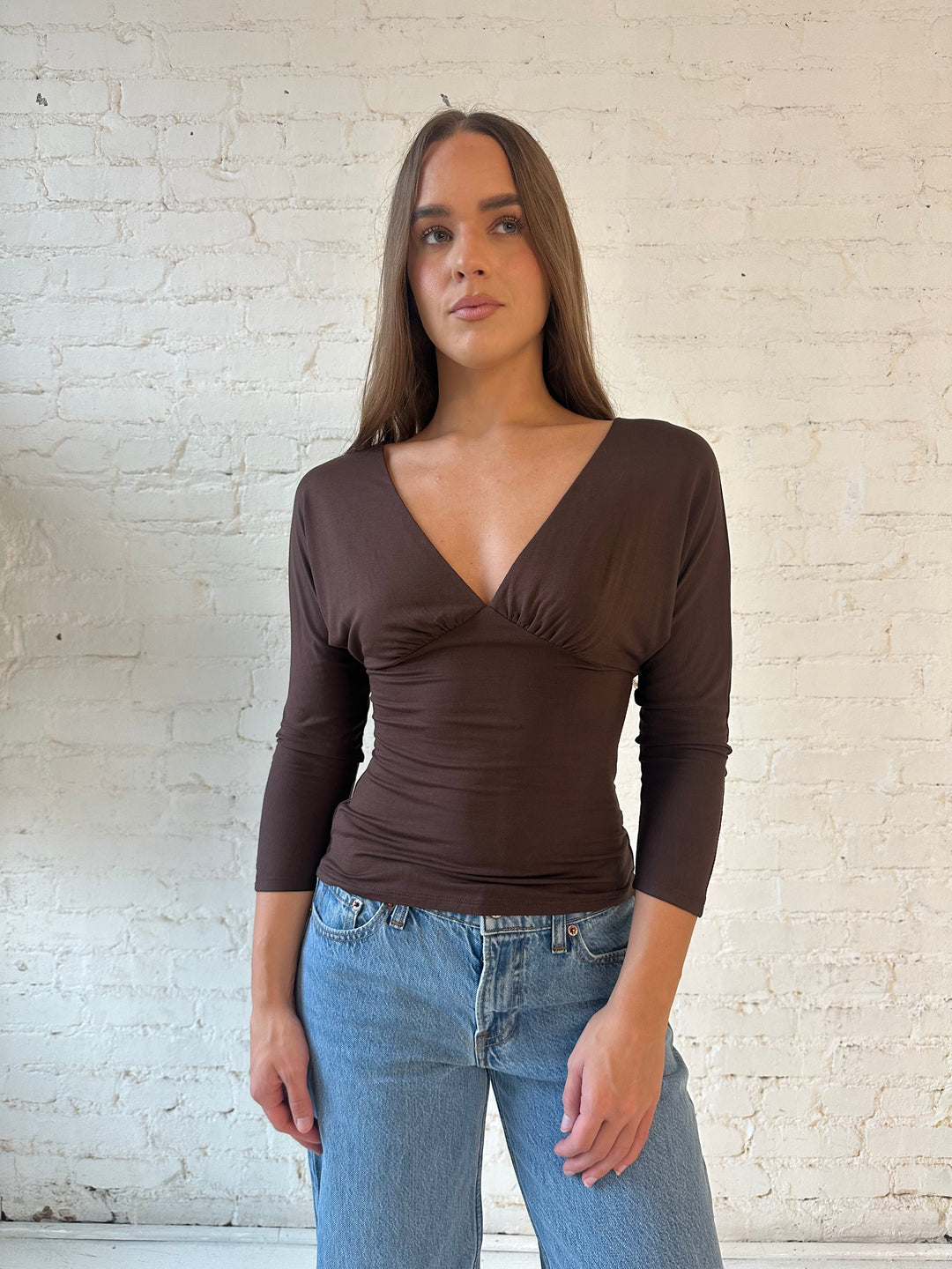 Woman wearing brown 3/4 sleeve top with medium wash jeans. 