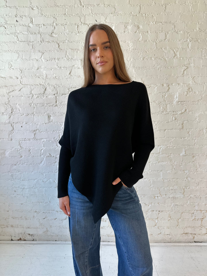 Woman wearing black ribbed long sleeve sweater with pointed hem, and dark wash jeans. 